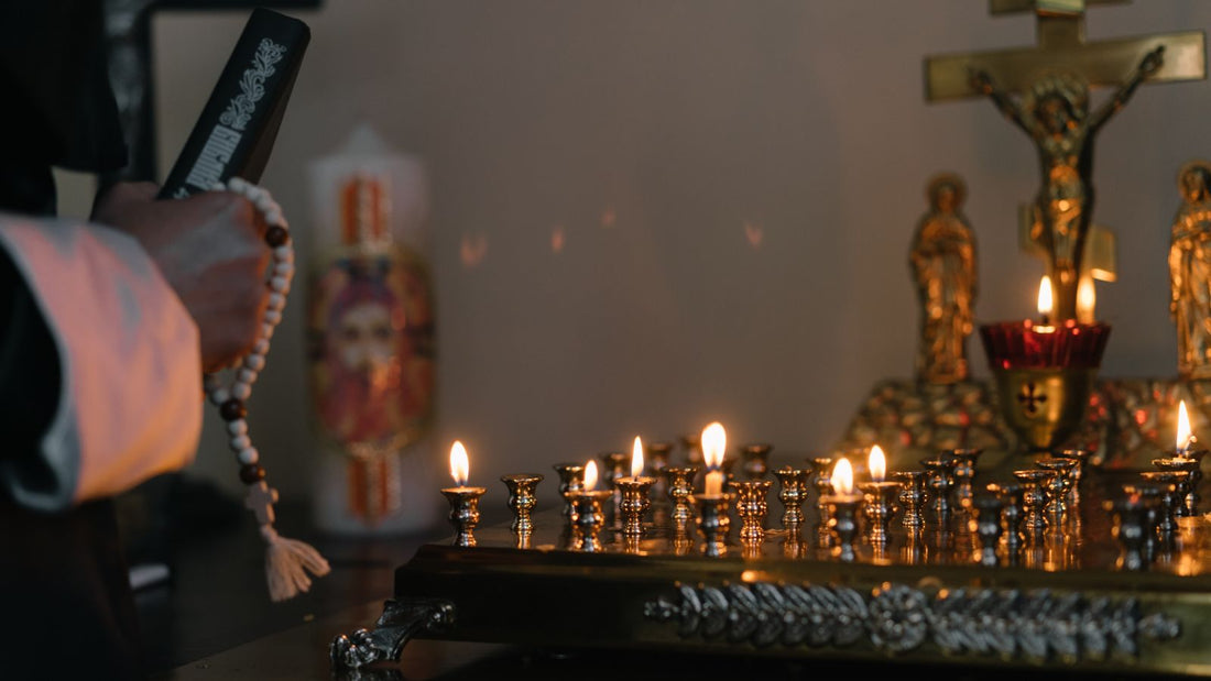 Un chapelet tenu à la main devant un présentoir de cierges allumés, dans une église.