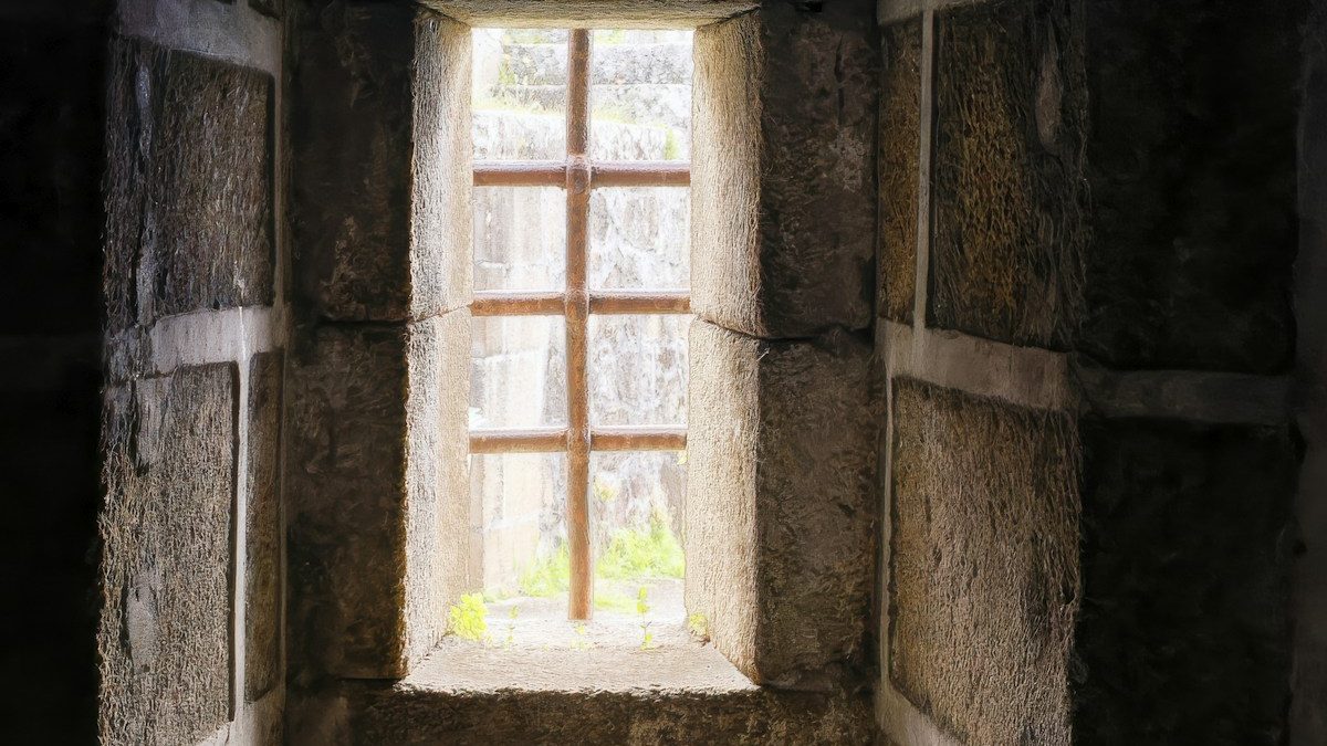 Fenetre profonde percee dans un mur de pierre nue, sa tablette de pierre claire eclairee par la lumiere du dehors