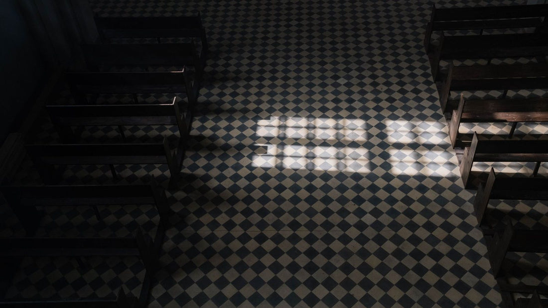 Rectangle de lumière projeté par une fenêtre sur le dallage d'une église vide, entre deux rangées de bancs