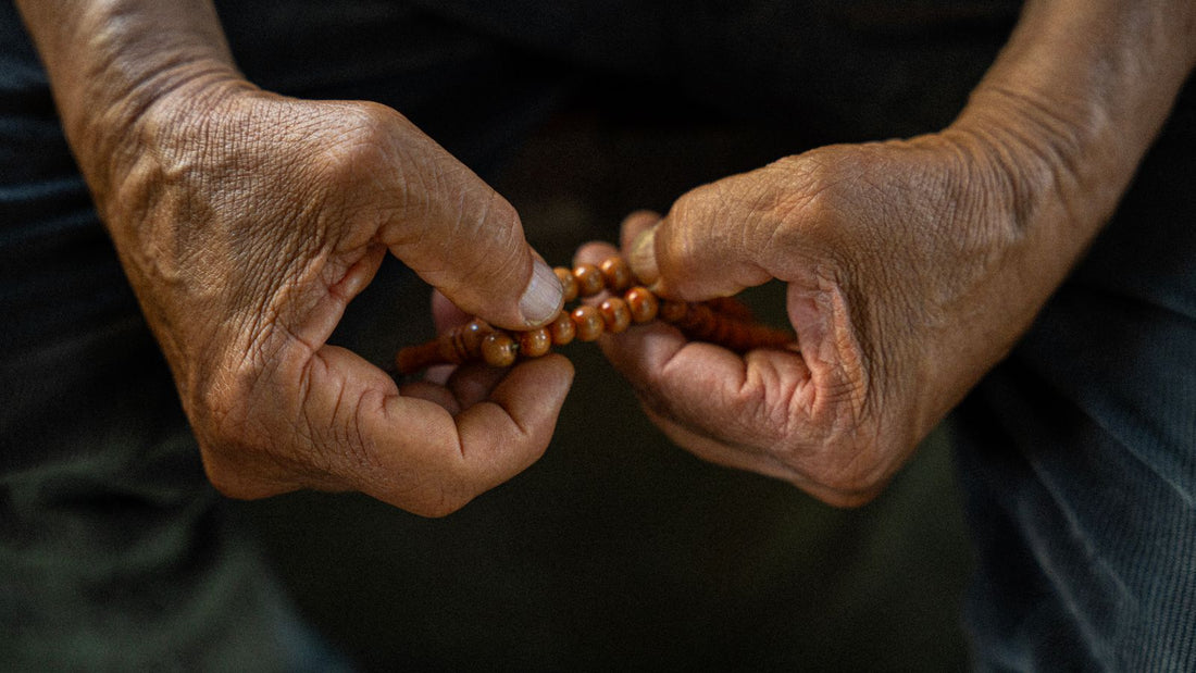 Deux mains âgées font glisser les grains de bois d’un chapelet, en gros plan.