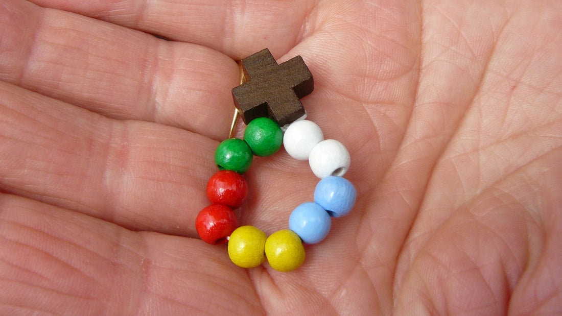 Petit dizainier de dix grains de bois colores termine par une croix de bois, tenu au creux d'une main