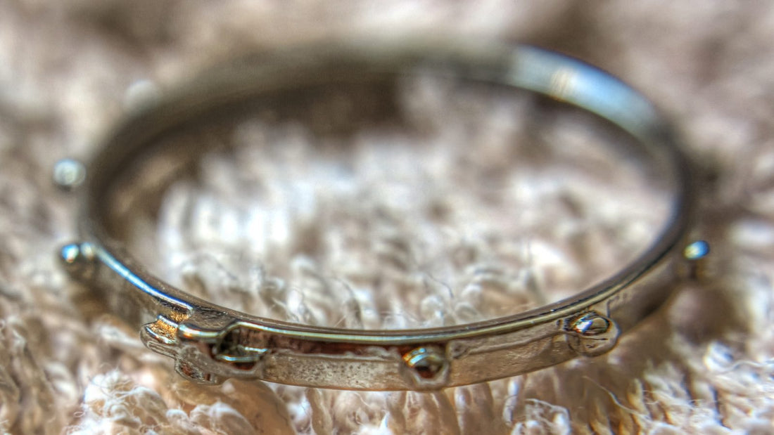 Anneau de chapelet en argent pose a plat sur un tissu ecru, ergots en relief sur le tour et petite croix sur le bord