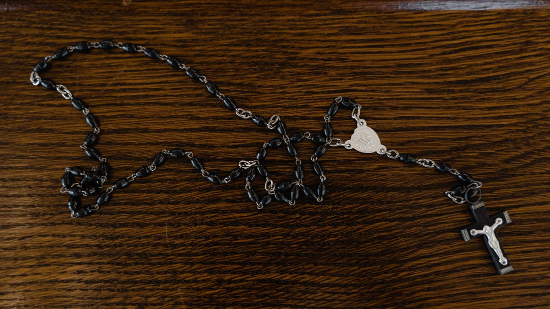 Chapelet catholique a grains noirs et crucifix, pose a plat sur une table en bois sombre