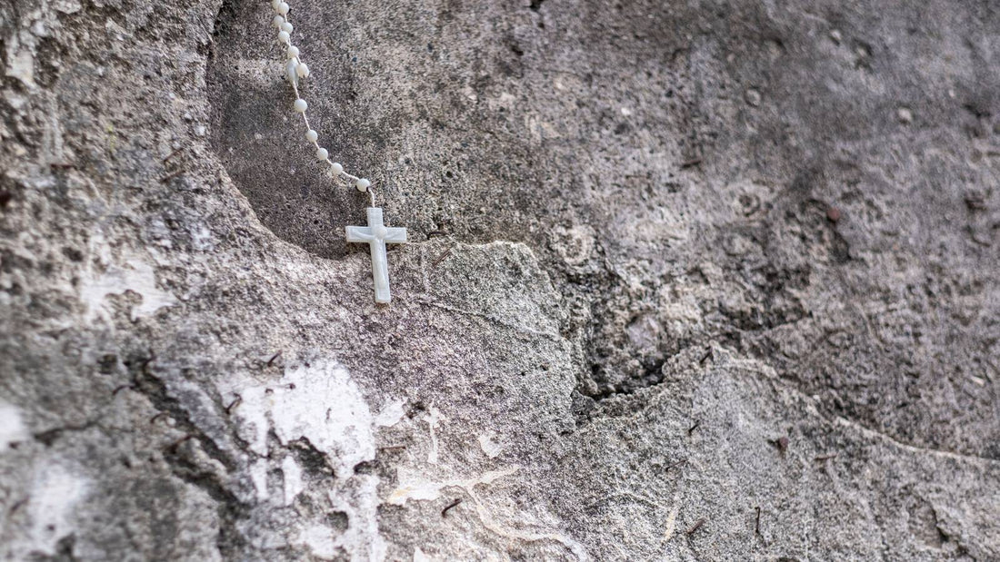 Chapelet de nacre claire et sa croix poses contre un mur de pierre usee et nue