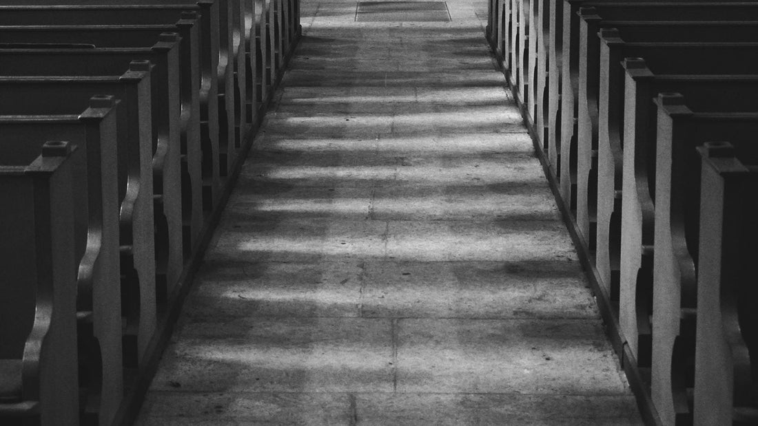 Allee centrale d'une eglise entre deux rangees de bancs de bois, le sol traverse par les bandes de lumiere regulieres venues des fenetres
