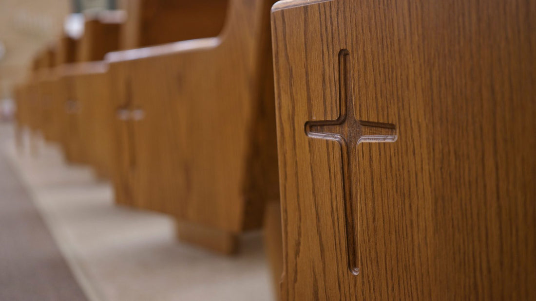 Joues de bancs d'eglise en bois, une croix creusee dans chaque panneau, la rangee se repetant jusqu'au fond, un vitrail hors focus au loin