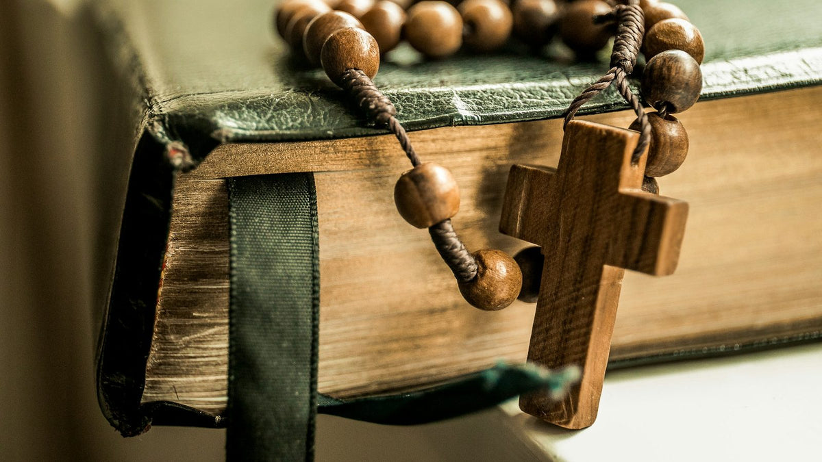 Chapelet en grains de bois pose sur la tranche d'un livre relie de cuir vert, a cote de son ruban marque-page.