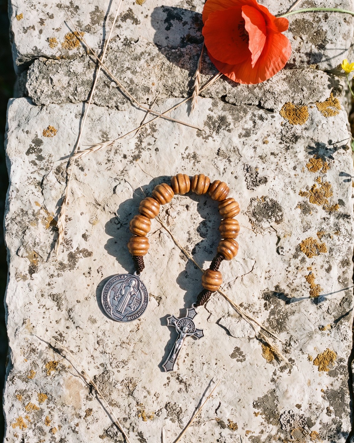 Le dizainier de poche Loculus, en bois, posé sur un muret de pierre sèche au soleil du matin, près d'un coquelicot.